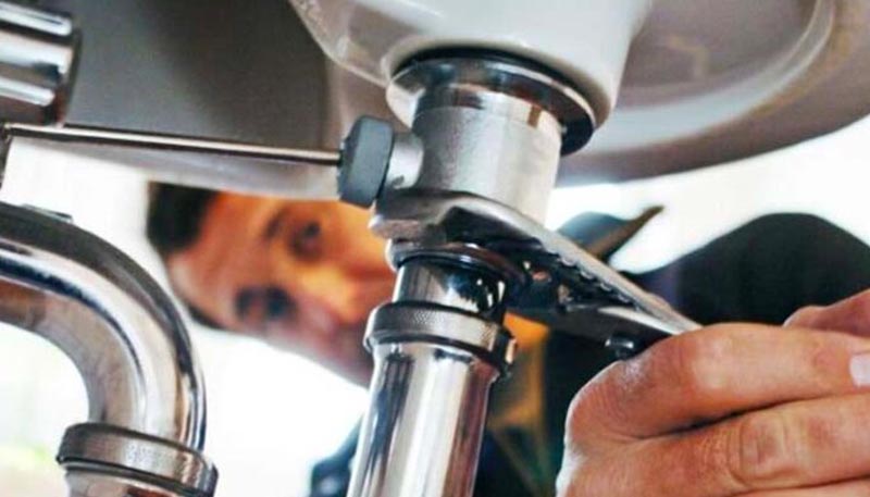 man using wrench under sink